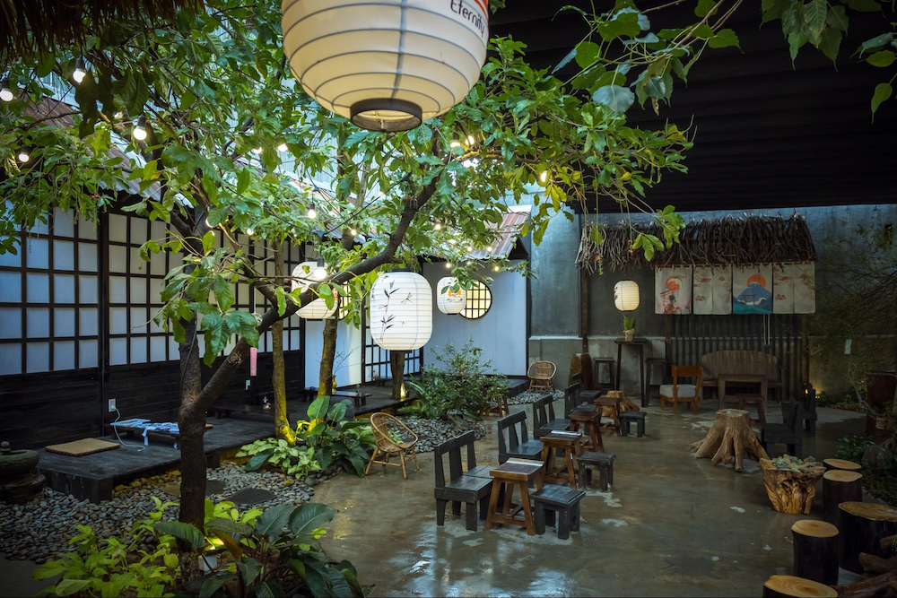 Những chiếc đèn lồng trắng nhẹ nhàng đung đưa trong gió, bàn ghế gỗ nhỏ xinh xếp dưới tán cây xanh mát, mang đến cảm giác bình yên như lạc vào một góc Kyoto giữa lòng phố thị