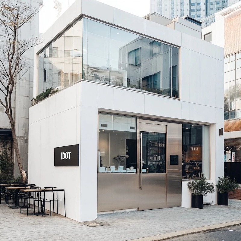Mẫu thiết kế quán cafe 2 tầng sử dụng tông màu trắng nổi bật, kết hợp với cửa ra vào kim loại mang lại cảm giác hiện đại, tân tiến.