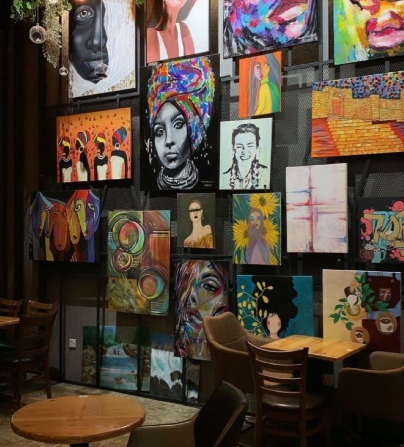 Quán cà phê được trang trí bằng tranh phong cách kết hợp giữa Expressionism và Abstract, với nét vẽ tự do và gam màu đậm, tạo nên không gian đầy cá tính và giàu cảm xúc 