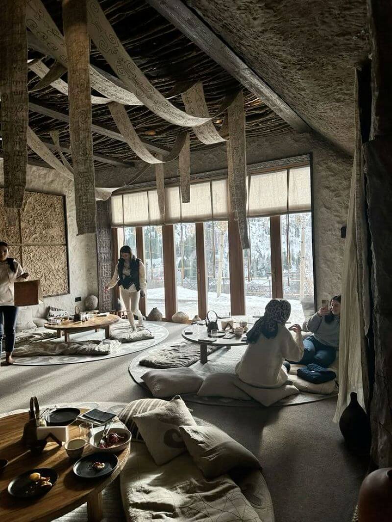 Một quán cà phê ngồi bệt phong cách rustic-minimal với đệm, bàn trà thấp, rèm tre, ánh sáng ấm và tông màu đất