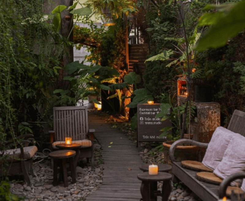 Không gian quán cafe sân vườn được thiết kế như một khu vườn nhỏ kín đáo, với lối đi bằng gỗ uốn lượn xuyên qua nền sỏi – tạo cảm giác gần gũi và yên bình