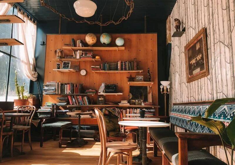 Không gian quán cà phê kết hợp giữa sự ấm cúng của thư viện và nét vintage cổ điển với điểm nhấn là bức tường gỗ với giá sách lớn