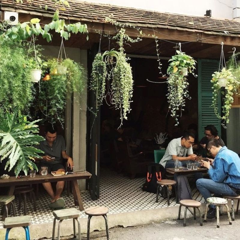 Quán cafe sân vườn nhỏ nằm gọn trong sân trước nhà, với những hàng cây xanh mát và bộ bàn ghế mộc mạc, tạo nên không gian thư giãn cho bất kỳ ai ghé qua