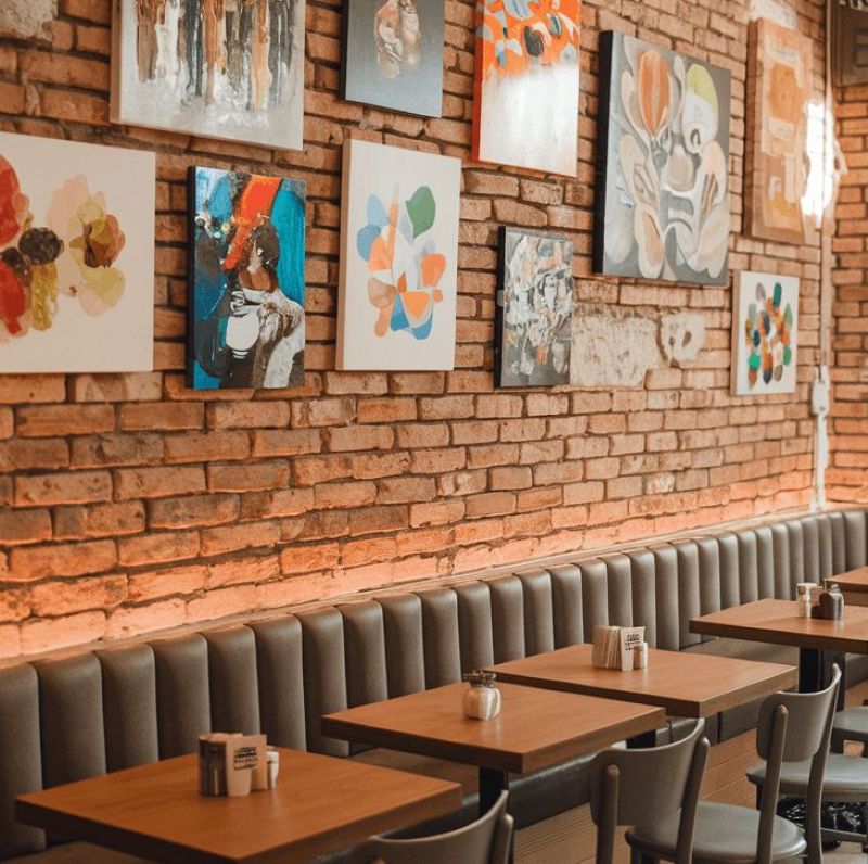Một bức tường gạch nung thô mộc mạc được điểm xuyết bằng những bức tranh trừu tượng đầy màu sắc, tạo nên sự đối lập thú vị giữa nét thô ráp tự nhiên và tính nghệ thuật hiện đại 