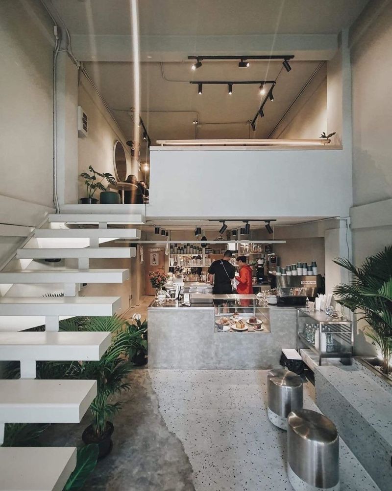 Thiết kế quán cafe gác lửng tập trung vào không gian mở, sử dụng tone trắng xám làm chủ đạo và điểm xuyết thêm vài cây xanh tạo cảm giác thư giãn 