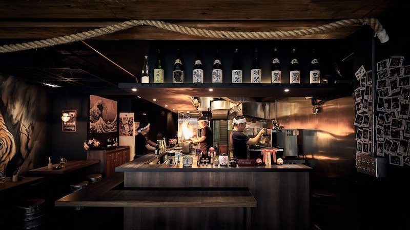 Quầy bar trong nhà hàng Nhật Bản phong cách Izakaya là trung tâm, nơi khách tương tác với đầu bếp và bartender, đồng thời tạo điểm nhấn thị giác 