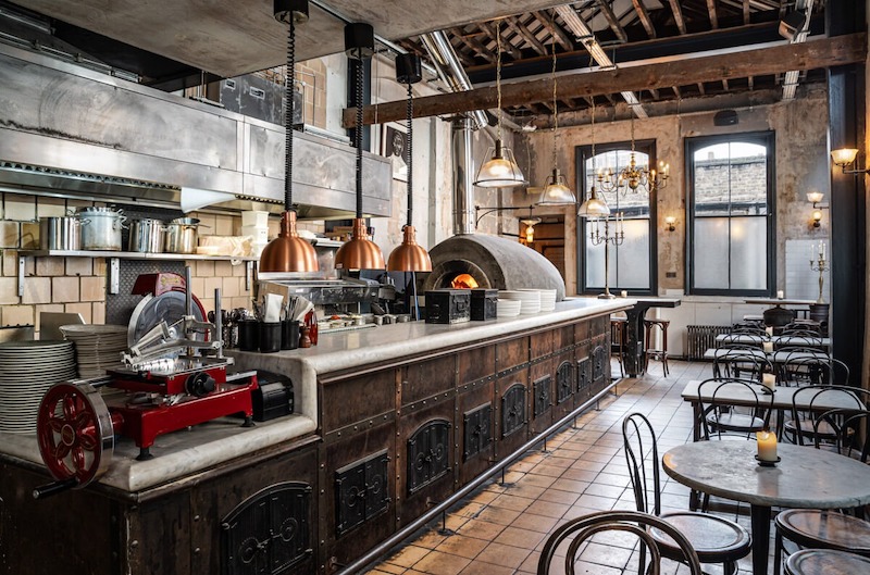 Quán pizza phong cách công nghiệp nổi bật với vật liệu thô mộc như bê tông, gạch thô, thép và kim loại, tạo không gian mạnh mẽ, cá tính và hiện đại 