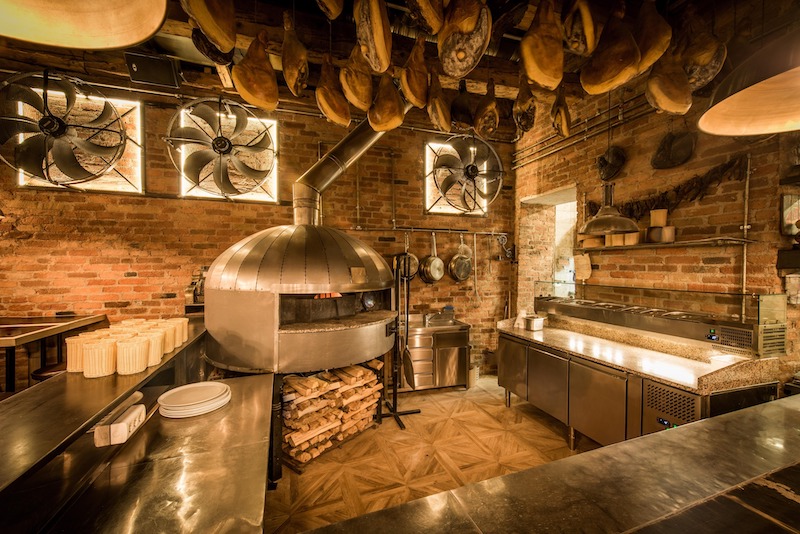 Hồn cốt của một quán pizza Ý truyền thống nằm trọn vẹn ở sự giao hòa giữa kiến trúc mộc mạc (Rustic) và bầu không khí ấm cúng kiểu gia đình 