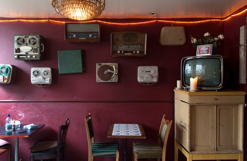 Mảng tường trưng bày radio và tivi cổ, kết hợp ánh đèn vàng và đồ gỗ cũ tạo cảm giác hoài niệm, ấm áp 