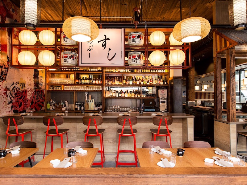 Quầy bar trung tâm kết hợp đèn lồng treo, ghế cao màu đỏ và kệ trưng bày rượu tạo điểm nhấn sôi động, đậm chất Á Đông 