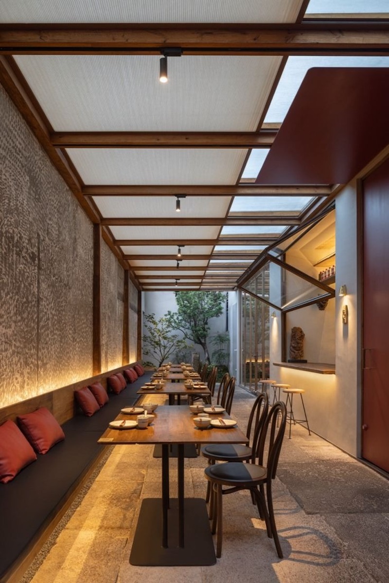 Dãy bàn dài bố trí dọc theo lối đi bán ngoài trời, kết hợp mái kính lấy sáng, ghế băng sát tường và cây xanh tạo cảm giác thoáng đãng, thư giãn 