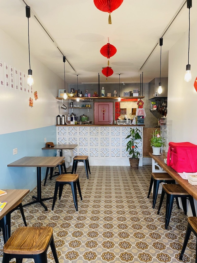 Bàn ghế gỗ đơn giản kết hợp gạch bông hoa văn, quầy phục vụ ốp gạch thông gió và đèn lồng đỏ tạo cảm giác gần gũi
