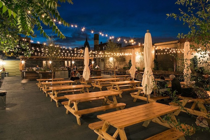 Những dãy bàn picnic gỗ đặt giữa sân rộng, dây đèn treo giăng cao tạo nên bầu không khí tụ họp ngoài trời rộn ràng mà gần gũi