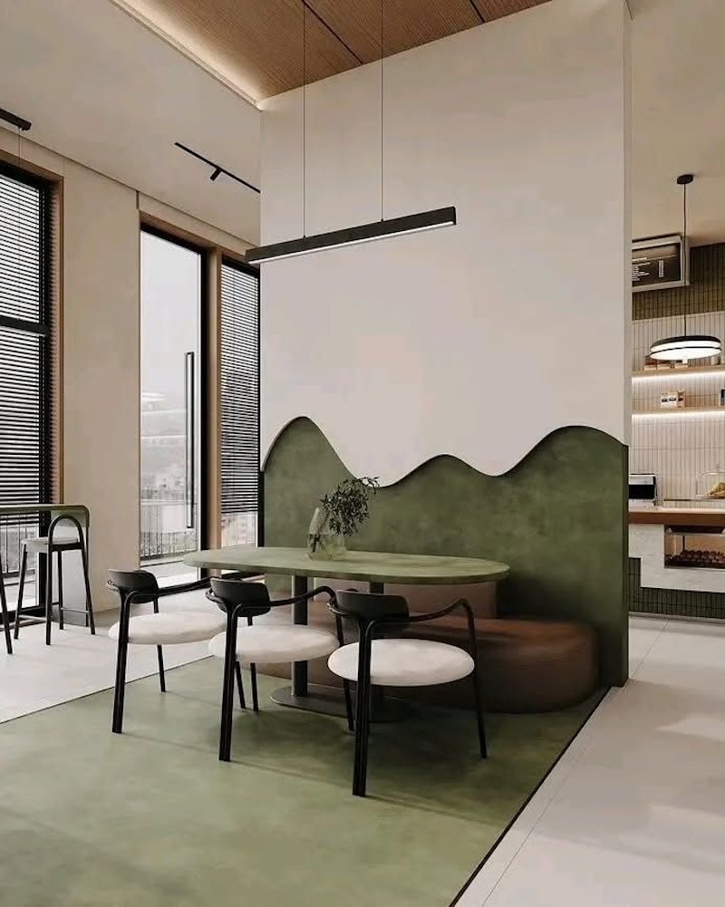 Khu vực ngồi được tạo hình liền khối với vách cong màu xanh olive, kết hợp bàn ghế tối giản và ánh sáng tự nhiên từ cửa kính lớn 