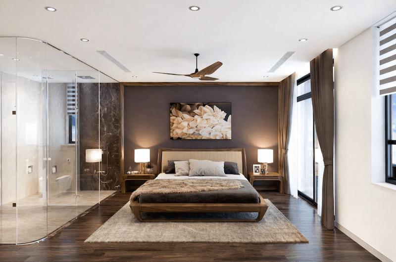 Giường gỗ thấp kết hợp bảng màu trầm ấm và phòng tắm kính liền kề, tạo cảm giác thư giãn như không gian nghỉ dưỡng riêng tư