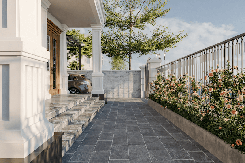 Lối vào biệt thự được tổ chức gọn gàng với bậc tam cấp ốp đá, sân lát đá chống trượt và hàng rào cây xanh chạy dọc, tạo khoảng đệm riêng tư
