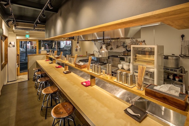 Thiết kế quầy bar truyền thống, sử dụng vật liệu gỗ mộc mạc và ánh sáng vàng ấm cúng, phù hợp cho mô hình nhà hàng Sushi đường phố diện tích nhỏ