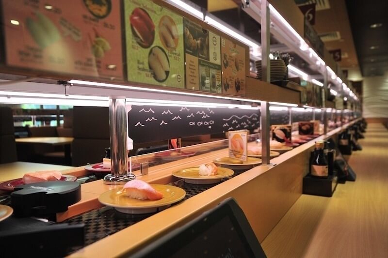 Các dải đèn LED âm tủ tập trung ánh sáng trực tiếp vào đĩa sushi trên đường ray, giúp làm nổi bật độ tươi ngon và màu sắc tự nhiên của thực phẩm