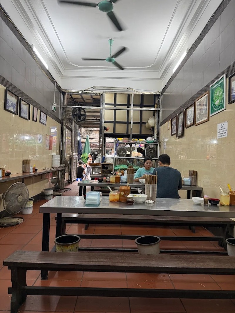 Không gian quán mang đặc trưng phở truyền thống Hà Nội với nhà ống sâu, bàn inox dài, tường gạch men, quạt trần, bố cục đơn giản ưu tiên công năng và phục vụ nhanh 