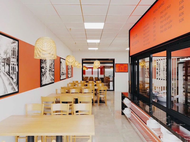 Không gian quán phở được thiết kế hiện đại theo dạng nhà ống, tông cam – trắng nhận diện thương hiệu, bàn ghế gỗ đồng bộ, bố cục thẳng hàng, sạch sẽ, dễ vận hành 