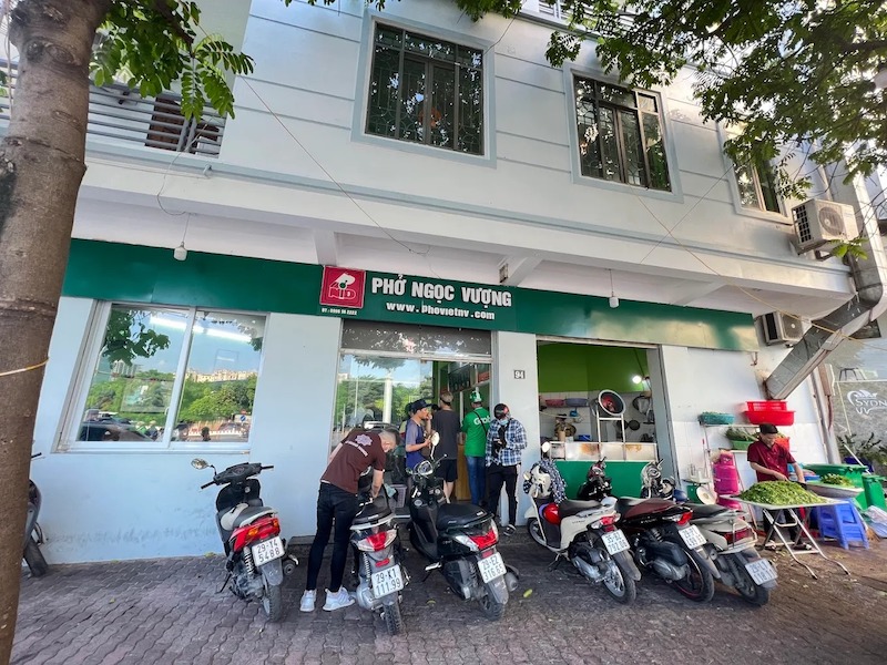 Biển hiệu xanh lục với chữ nổi trắng hiện đại trên nền tường cam, tạo sự tương phản mạnh mẽ và diện mạo chuyên nghiệp cho quán Phở Ngọc Vượng