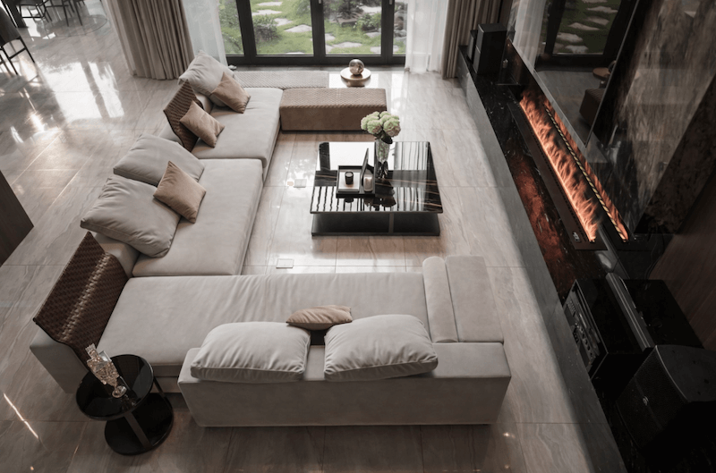 Phòng khách với bố cục sofa chữ U, gam màu trung tính, sàn đá khổ lớn và hệ cửa kính mở ra sân vườn, tạo cảm giác rộng rãi, sang trọng và kết nối liền mạch với không gian bên ngoài