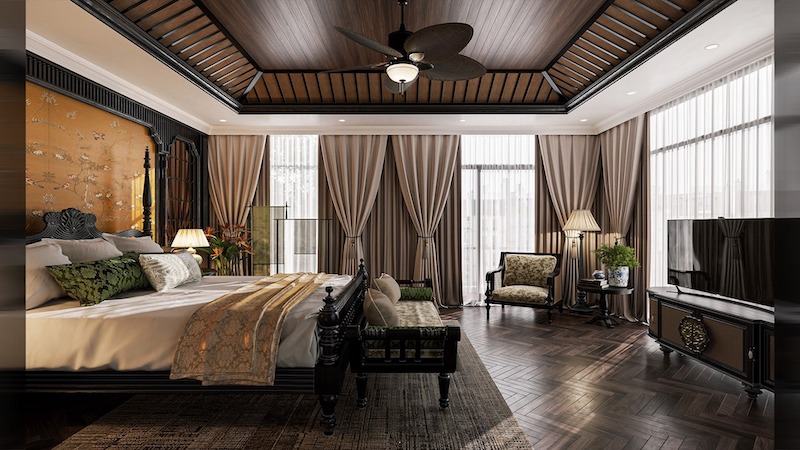 Giường gỗ chạm khắc tạo điểm nhấn trung tâm, trần nan gỗ kết hợp quạt trần cổ điển, rèm vải cao kịch trần và sàn xương cá tăng chiều sâu không gian Indochine