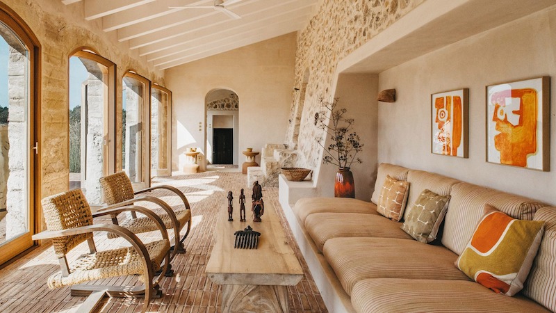 Hệ cửa kính khung gỗ mở rộng tầm nhìn, sofa built-in vải thô liền tường tạo cảm giác thư giãn, bàn gỗ nguyên khối nhấn mạnh tinh thần mộc mạc Địa Trung Hải