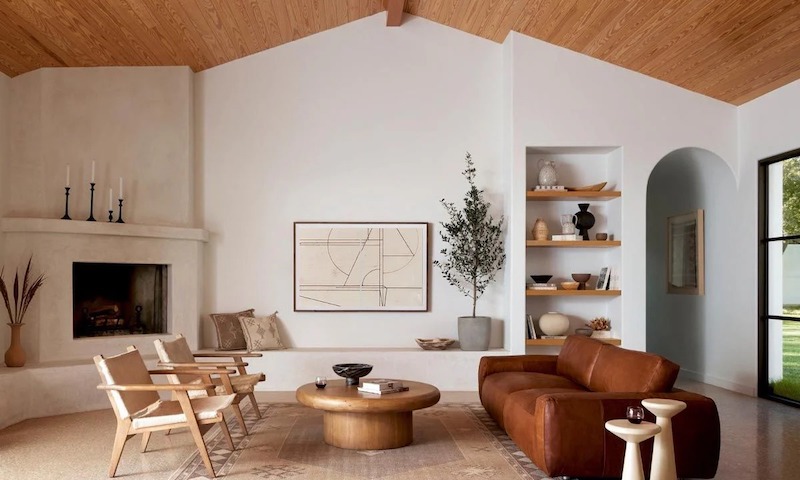 Sofa da nâu tạo điểm nhấn ấm áp, bàn trà tròn gỗ đặc giữ bố cục trung tâm, lò sưởi xây thô và kệ âm tường tôn tinh thần Địa Trung Hải