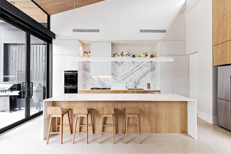 Thiết kế nhấn mạnh mảng trắng tinh gọn, đảo bếp lớn ốp đá vân tự nhiên, gỗ sáng màu và ánh sáng tuyến tính, tạo cảm giác thoáng đãng, hiện đại, cân bằng