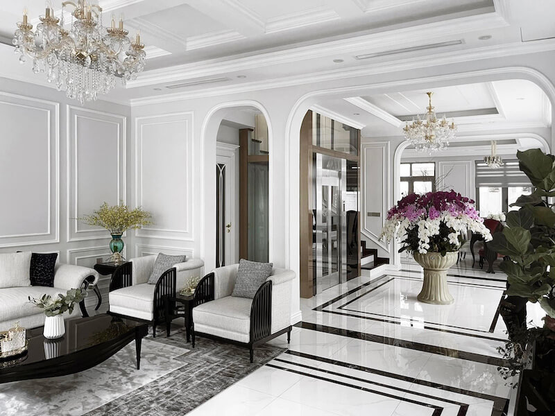 Không gian phòng khách tinh tế với phào chỉ tường trắng thanh lịch, đèn chùm pha lê lấp lánh và sàn marble bóng gương, tôn lên vẻ sang trọng, chuẩn mực vượt thời gian.