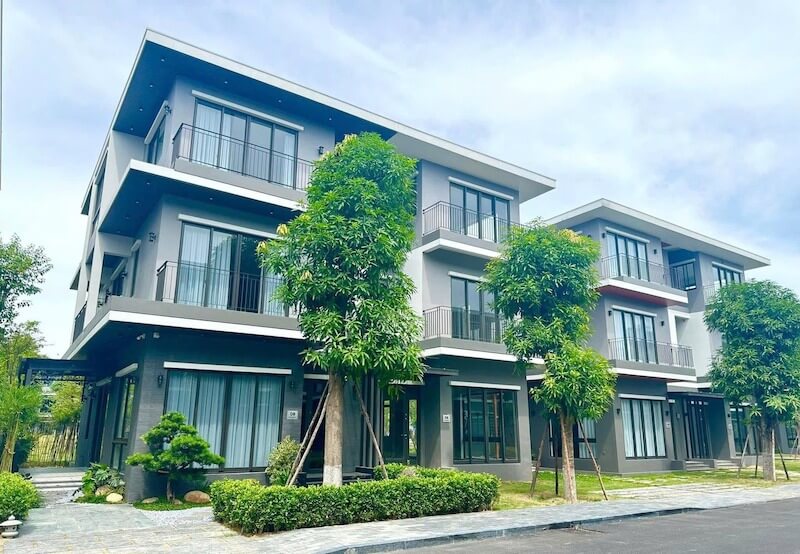 Thiết kế phong cách hiện đại nổi bật với mái bằng, ban công rộng, cửa kính lớn và mảng xanh bao quanh, tạo không gian sống thoáng đãng.