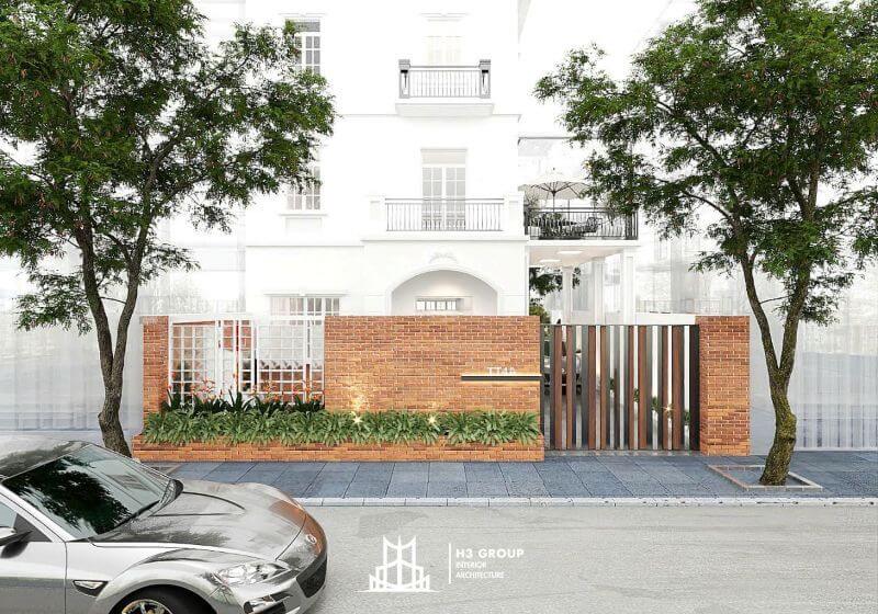 Mặt tiền biệt thự gây ấn tượng với tường trắng thanh lịch, ban công sắt tối giản và hàng rào gạch đỏ kết hợp cổng kim loại, tạo vẻ sang trọng, gần gũi