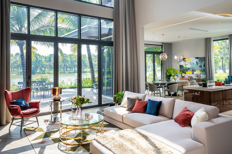 Hệ cửa kính cao kịch trần mở trọn tầm nhìn ra sông và hàng dừa xanh, đưa ánh sáng tự nhiên ngập tràn không gian sống