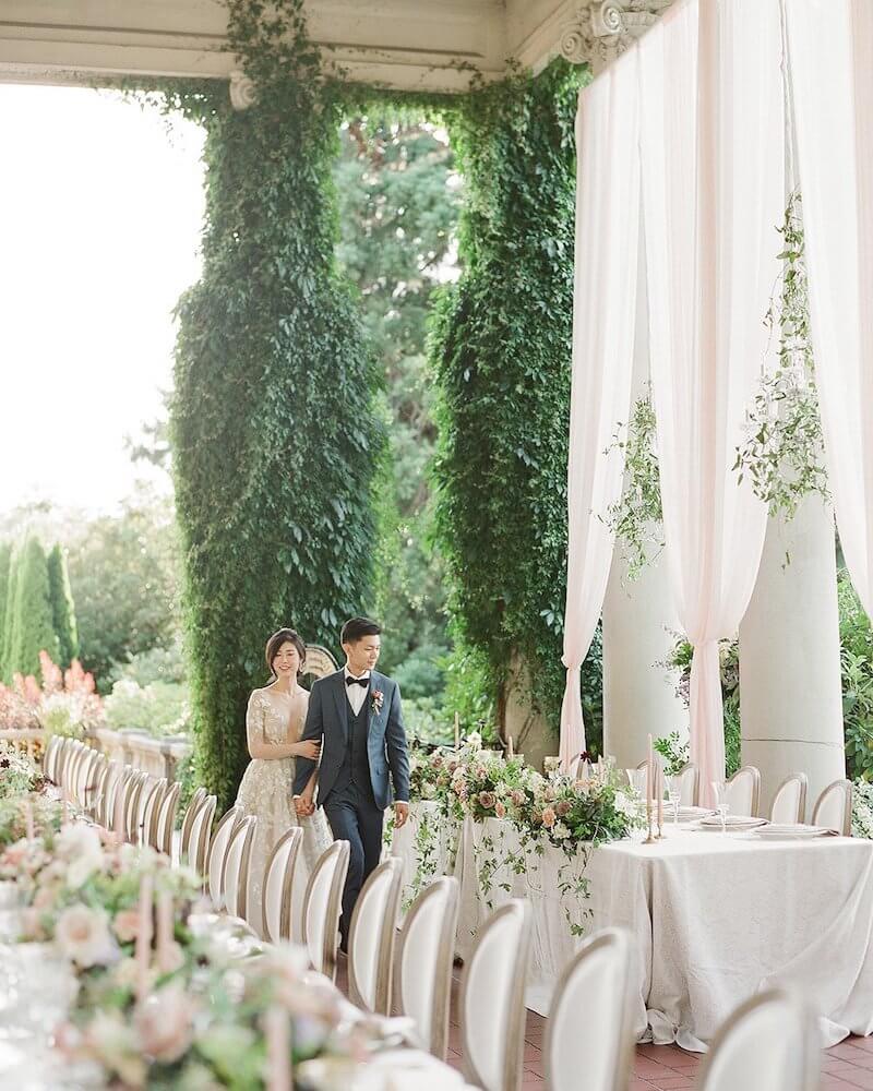 Không gian nhà hàng lãng mạn với cột phủ dây leo xanh mướt, rèm voan trắng mềm mại và bàn tiệc hoa pastel hài hòa giữa thiên nhiên