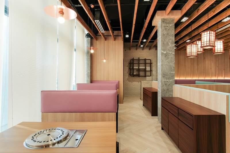 Không gian được xử lý theo phong cách tối giản ấm áp với vách gỗ sáng màu, ghế băng bọc nệm hồng pastel và trần nan gỗ tạo chiều sâu, mang lại cảm giác riêng tư