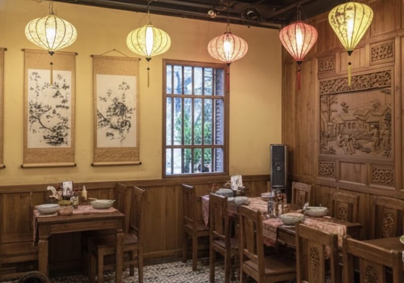 Góc ngồi nhỏ sử dụng bàn ghế gỗ mộc kết hợp tường ốp gỗ chạm và tranh thủy mặc, tạo cảm giác gần gũi, đậm chất truyền thống