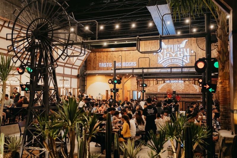 Không gian sôi động với bố cục mở, ánh đèn trang trí treo trần kết hợp vật liệu gỗ - kim loại thô mộc, tạo cảm giác gần gũi và giàu năng lượng