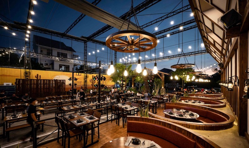 Không gian mang phong cách công nghiệp với khung thép lộ kết cấu, đèn thả ánh vàng ấm, tạo cảm giác phóng khoáng nhưng vẫn ấm cúng về đêm