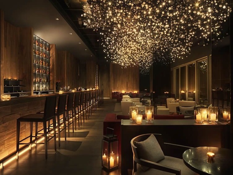 Thiết kế ánh sáng phân lớp trong không gian quầy bar của nhà hàng sang trọng, ánh sáng hắt chân quầy bar và nến trang trí tạo chiều sâu không gian