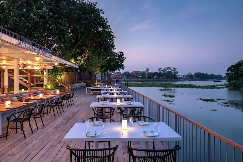 Không gian nhà hàng ven sông được bố trí theo kiểu terrace ngoài trời với sàn gỗ rộng, bàn ghế tối giản và lan can mở hướng ra mặt nước