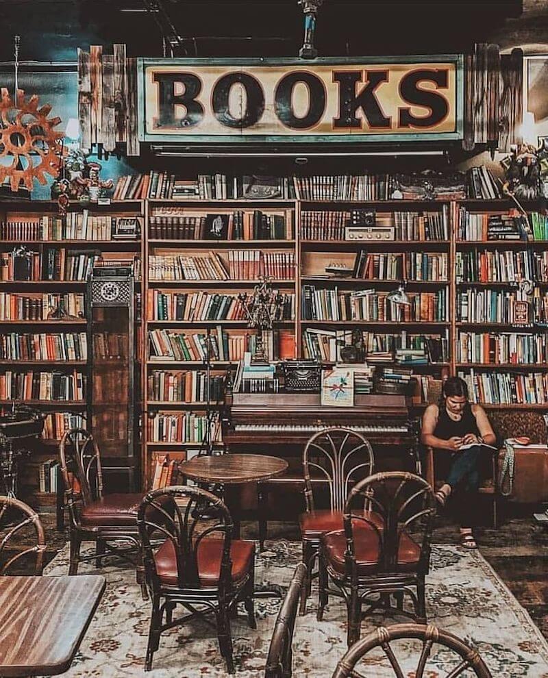 Kệ sách gỗ tối màu với bề mặt hơi sờn, kết hợp ánh sáng vàng tạo cảm giác hoài cổ, ấm áp cho không gian đọc thư giãn