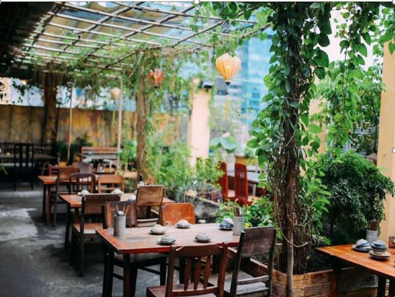 Sự kết hợp giữa bàn ghế gỗ cũ kỹ và giàn cây leo xanh mướt mang lại cảm giác bình yên, hoài niệm và thư thái như đang lạc vào một góc vườn xưa giữa lòng phố thị