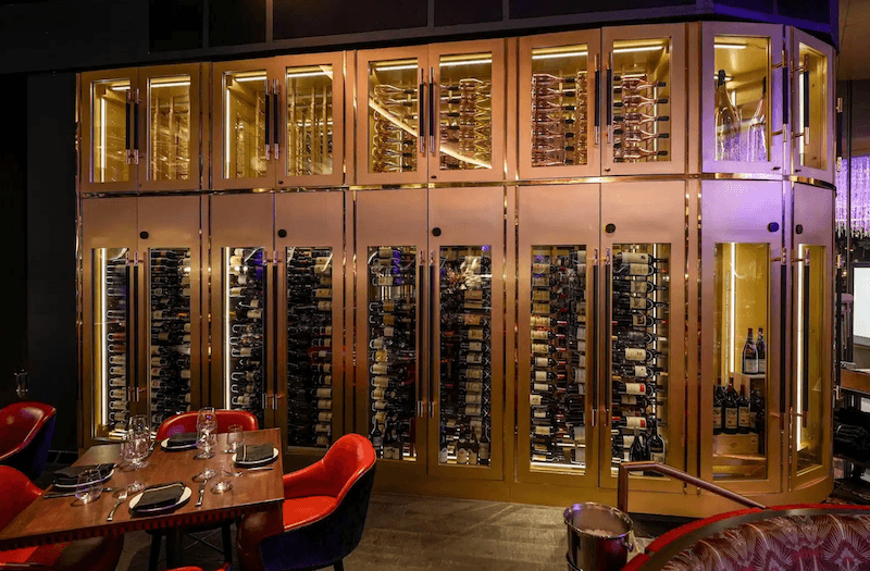 Tủ rượu vang cỡ lớn được thiết kế như một điểm nhấn trung tâm của không gian steakhouse, với hệ tủ kính cao kịch trần và đèn LED hắt sáng sang trọng