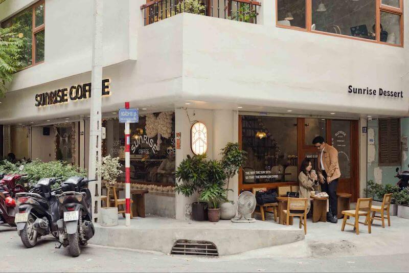 Việc sử dụng bàn ghế gỗ mộc mạc đặt tại khu vực vỉa hè góc phố tạo nên một không gian mở gần gũi, mang đậm chất thư thái nhẹ nhàng